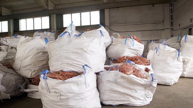 huge white bags with copper scrap from wires are lying in a warehouse of scrap metal processing plant