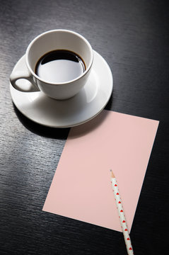 coffee, pink paper and pen on a black table