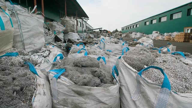 shredded metal garbage is packing in large white plastic bags, laying on a ground outdoor in a wrecking yard in daytime