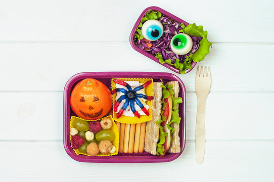 Open Halloween lunch box with sandwich, mandarin, berries and vegetable salad on white background with blank space for text
