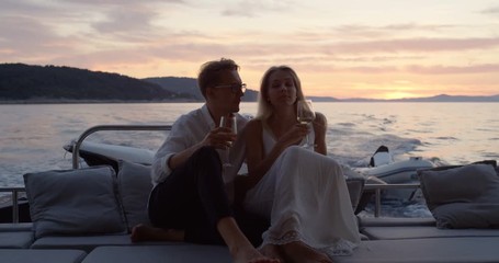 Young Couple Hug, Drink Champagne in the Stern of the Moving Yacht. They Have Great Romantic Evening. In the Background Island with Small Village. Shot on RED Epic 4K UHD Camera.