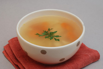 Spicy homemade soup served in pottery bowl with orange napkin on gray background