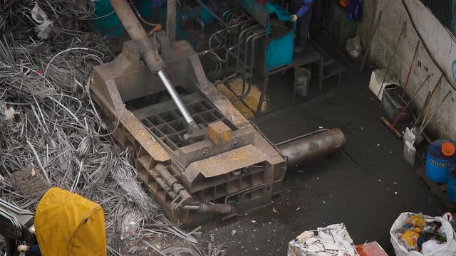 pressing machine is compressing metal scrap in a wrecking yard of scrap processing plant, outdoors in daytime