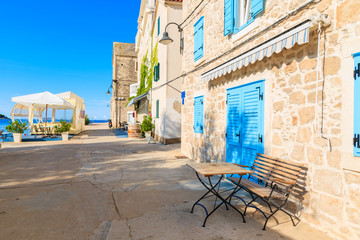 Small table in front of coastal restaurant with blue windows old town of Primosten, Dalmatia, Croatia - obrazy, fototapety, plakaty