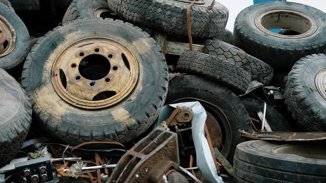old rusty wheels of different vehicles are dumped in a heap in a territory of waste processing plant in daytime