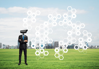 Camera headed man standing on green grass against modern cityscape