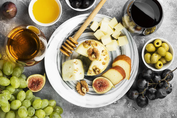 Snacks with wine - various types of cheeses, figs, nuts, honey, grapes on a gray background. Top view. Food background