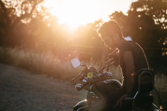 Man sitting on his motorbike on a country road at sunset