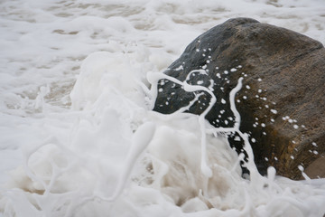 Ocean waves crash on beach shore rock create foam over sand.