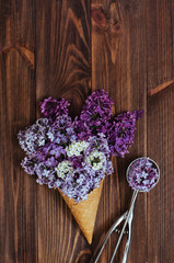 Fototapeta na wymiar Ice cream waffle cone with lilac flowers and spoon