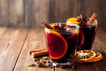 Two glasses of christmas mulled wine with oranges and spices on wooden background. - obrazy, fototapety, plakaty