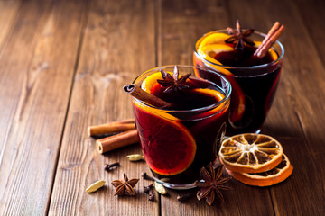 Two glasses of christmas mulled wine with oranges and spices on wooden background.