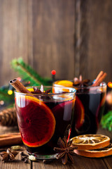Two glasses of christmas mulled wine with oranges and spices on wooden background.