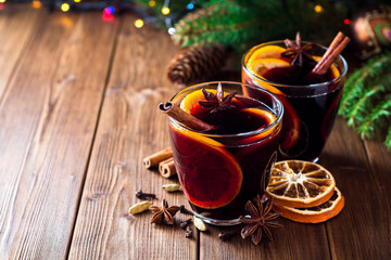 Two glasses of christmas mulled wine with oranges and spices on wooden background.