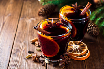 Two glasses of christmas mulled wine with oranges and spices on wooden background.