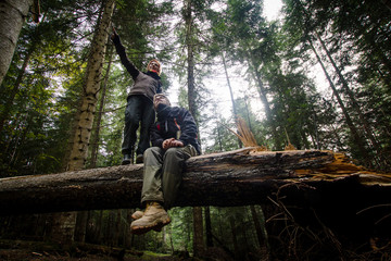 young hikers couple having good time in forest, sitting on old fallen tree 
