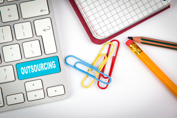 Outsourcing concept. Computer keyboard on a white office desk with various items.