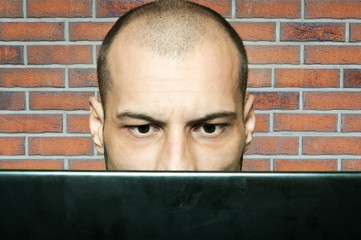 Confused bald man staring at his computer monitor while he is sitting in his office with red brick...