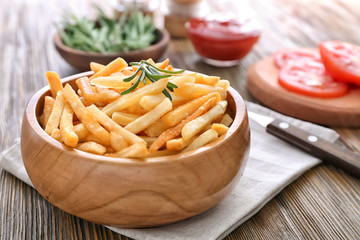 Bowl with yummy french fries on wooden table
