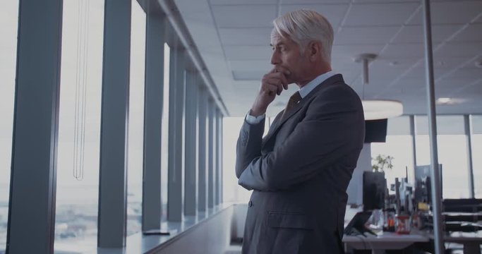 Side view shot of mature businessman standing in office and looking outside the window. Male entrepreneur standing in office and thinking.