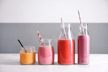 Glassware with different smoothies on table against color background