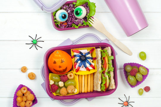 Open Halloween lunch box with school lunch on white wooden background