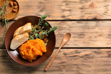 Plate with mashed sweet potato and bread on wooden background