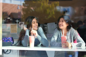 Two teen girls at outdoor cafe drinking boba tea together