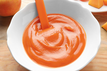 Ceramic bowl with baby food on wooden background
