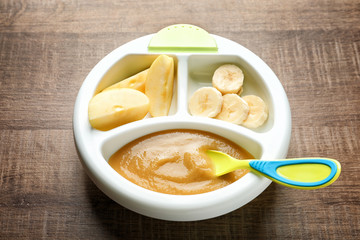 Section plate with baby food and fresh fruits on wooden background