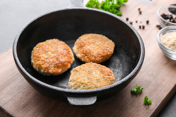 Frying pan with salmon patties on wooden board