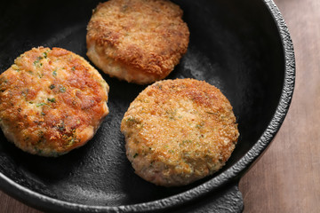 Frying pan with salmon patties on wooden board, closeup