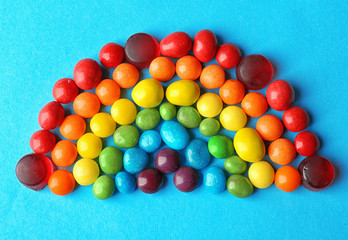 Colorful candies arranged as rainbow on blue background