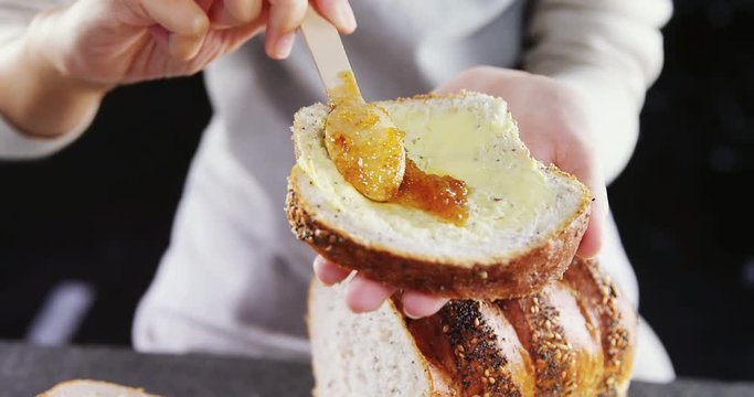 Woman applying jam over multigrain bread slice 