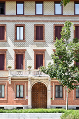 Fototapeta na wymiar Front view of a beautiful facade of a building in Milan, Italy, with a young tree growing next to the building entrance