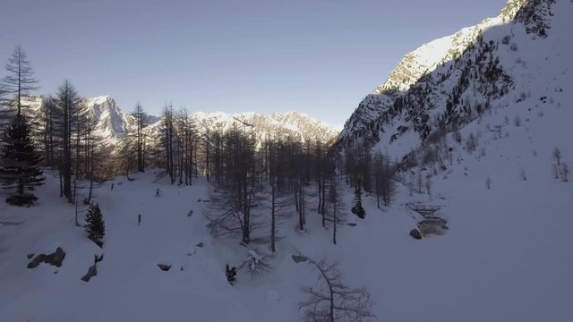 Aerial drone flight establisher over iced lake with skier and snowy forest. Winter snow in mountain nature outdoors. Travel exploring Alps. 4k video forward