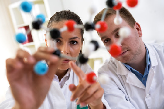 Two students of chemistry looking at molecular model and making new formula at laboratory