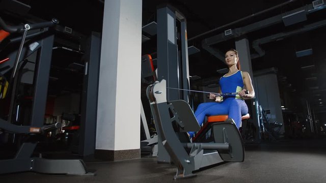 Pretty girl bodybuilder training hands and back exercising on weight-lifting training machine and press workout in gym