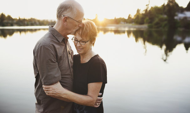 Content middle aged, retired couple hugging together outside on lake ocean dock