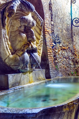 Obraz premium Antique fountain on the wall of Parco Savello in Aventine, also known as Orange Garden, Rome - Italy. Night view of the famous sculpture in marble and granite.