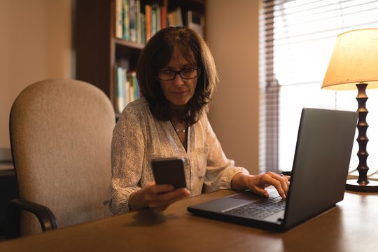 Woman using a mobile phone and laptop while sitting at home desk