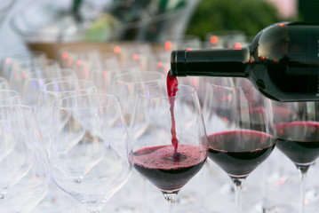 pouring red wine from a dark green bottle in wine glass close up white background