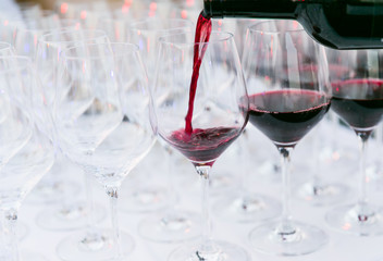pouring red wine from a dark green bottle in wine glass close up white background