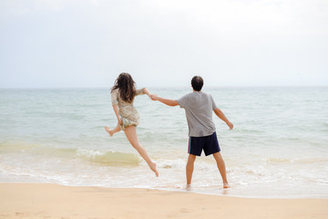 Fototapeta na wymiar Adult young happy jumping couple on seashore outdoors nature sand background. Back view of pretty romantic lovers having fun holding hands in tenderness bliss moment. destination trip