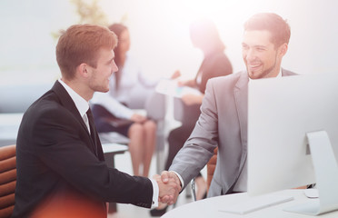 Fototapeta premium Two happy young men shaking hands while sitting at the office