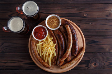Appetizing beer snacks plate. Grilled sausages and french fries served with tomato ketchup, mustard and dark beer. Oktoberfest food, pub concept