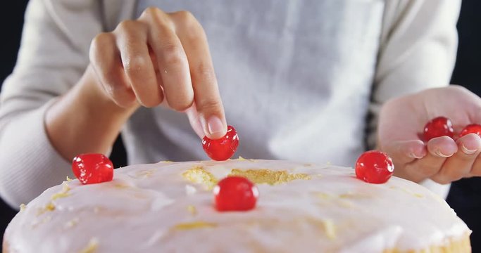 Woman topping a fresh baked cake with cherry 