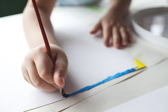 A young boy paints a rainbow at a table in the afternoon window light