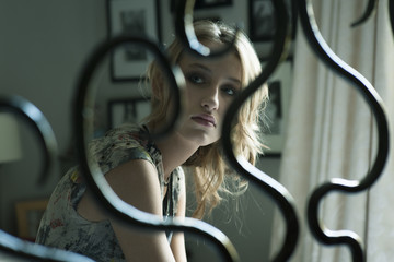 Young pensive 18 year old girl sitting in her bedroom and seen through her bed post