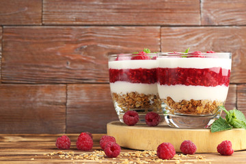 Dessert with raspberries and granola in glasses on brown wooden table